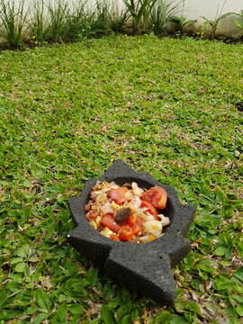 Fresh Indonesian sambal ingredients served in a traditional stone mortar on green grass background, perfect for culinary, organic food, and Asian cuisine themes.
