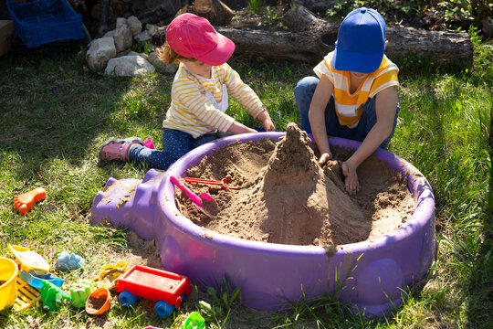 two children brother and sister play with sand in a sandbox in the garden on a summer day. Feral Kid Summer