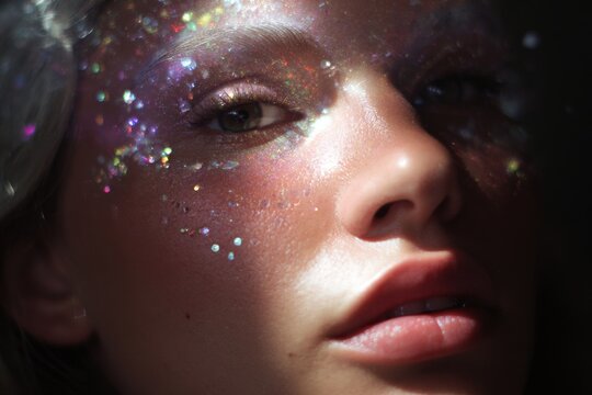 Close-up model face with scattered holographic crystals and glitter for festival makeup and party poster background