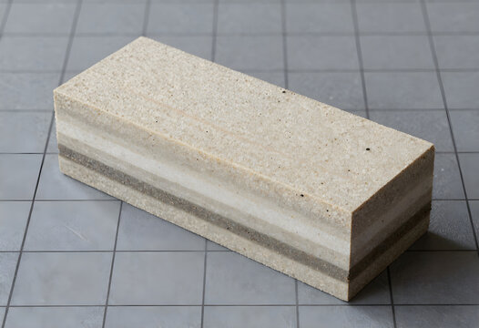 An isolated technical view of a single geopolymer block module showing distinct vitrified slag strata layers, resting over a high-contrast industrial grid.