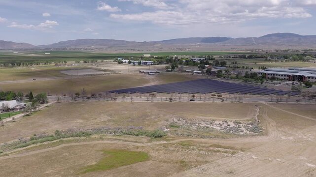Aerial drone view of a solar panel farm generating clean, renewable energy in the rural landscape of Minden, Nevada, with distant mountains under a partly cloudy sky during daytime