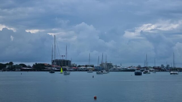 View over Simpson Bay in Sint Maarten on a calm overcast day, with sailing boats and catamarans anchored in tranquil water beneath dark storm clouds during hurricane season