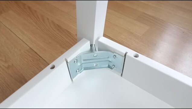 Assembly of a table frame by attaching a table leg with metal brackets, bolts and nuts. Furniture installation process focused on fastening structural components.