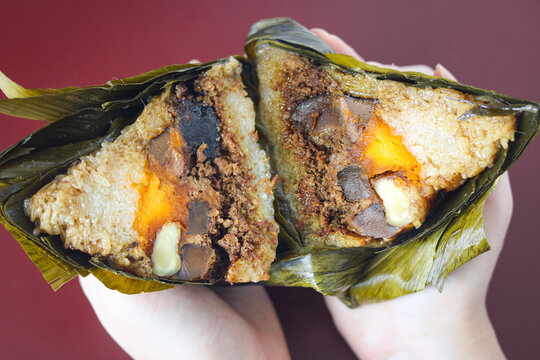 Hand holding a bacang (zongzi). This traditional Chinese sticky rice dumpling is wrapped in banana leaves.