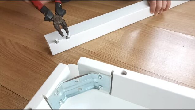 Assembly of a table frame by attaching a table leg with metal brackets, bolts and nuts. Furniture installation process focused on fastening structural components.