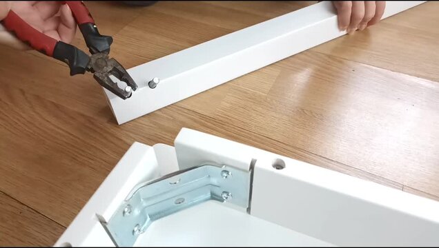 Assembly of a table frame by attaching a table leg with metal brackets, bolts and nuts. Furniture installation process focused on fastening structural components.