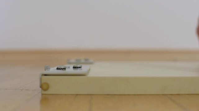 Closeup hinge on cabinet door on floor showing hardware and wood grain minimalist indoor scene with parquet floor, visible hinge plate and screws, static composition suggesting