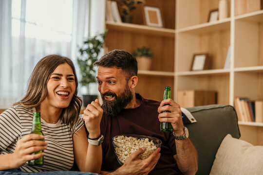 Couple enjoying home entertainment cheering drinking beer eating popcorn
