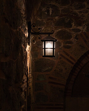 Old wall lantern glowing on a stone wall in a historic monastery interior
