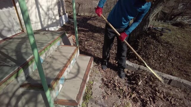 Man doing spring garden work and raking fallen leaves Garden pathway and yard cleanup scene during spring maintenance and preparation