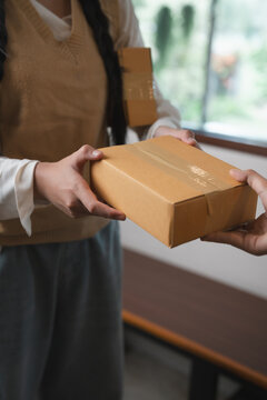 Entrepreneur handing over cardboard parcel box to customer during e-commerce package delivery and shipping logistics transaction process
