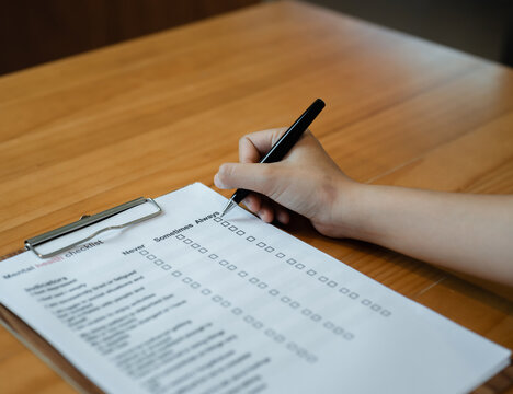 Person filling mental health checklist on clipboard with pen, psychological assessment, self evaluation, healthcare screening and wellbeing awareness concept.