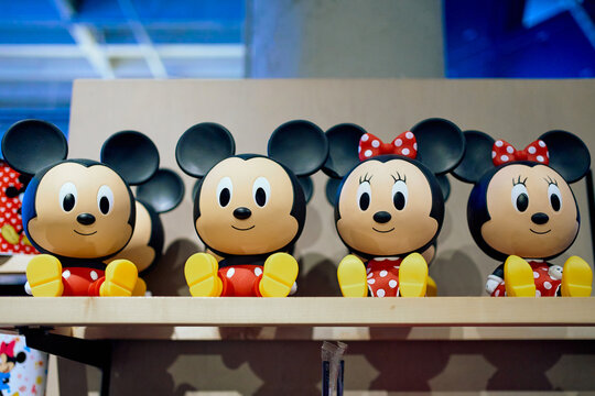 Cute Mickey Mouse and Minnie Mouse plastic figures sitting on a wooden display shelf in a Disney merchandise store.