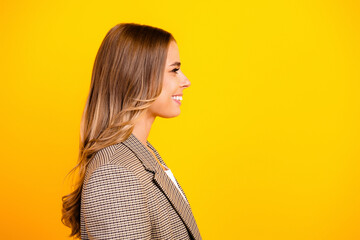 Young professional woman smiling in profile portrait against bright yellow background, wearing a checked blazer and long hair conveying confidence and optimism © deagreez