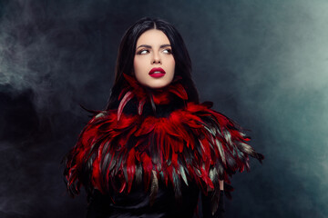 Fototapeta premium Mysterious elegant woman in red feather costume posing confidently against a smoky background
