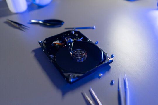A hard disk drive is opened on a table with small tools and equipment around it during a computer repair process