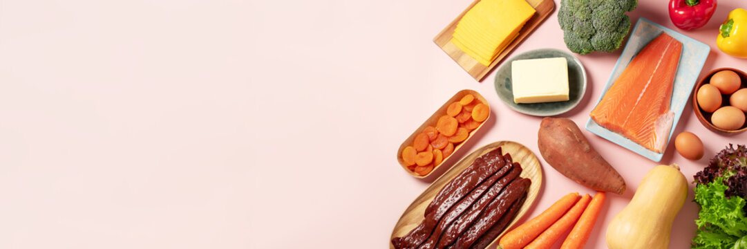 Border flat lay background with retinol rich foods and betacarotene ingredients on pink, web banner,