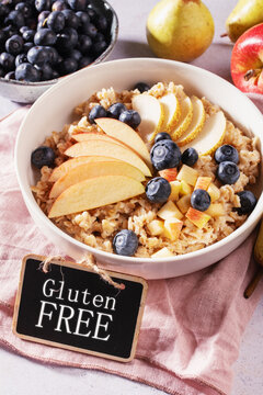 Bowl of oatmeal topped with apple, pear and blueberries with &ldquo;Gluten free&rdquo; text, healthy certified gluten free breakfast concept for celiac and wheat free lifestyle