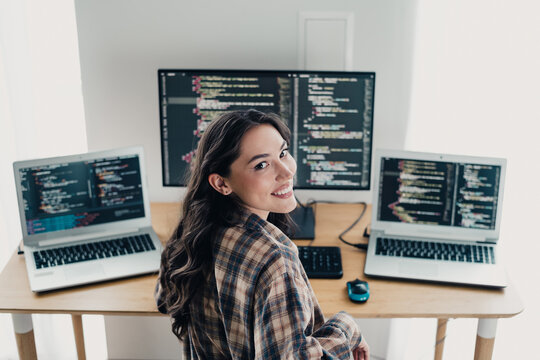 Female programmer smiling at her desk with multiple monitors coding in a bright home office workspace
