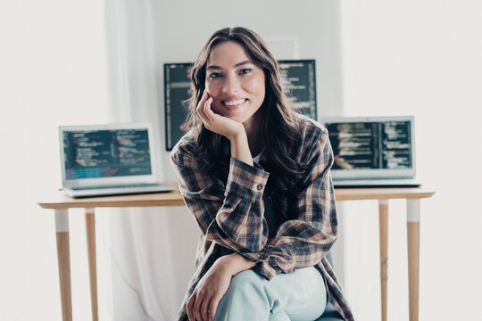 Smiling female developer working in a home office with laptops and code on multiple screens, relaxed web developer and software programmer at a casual desk