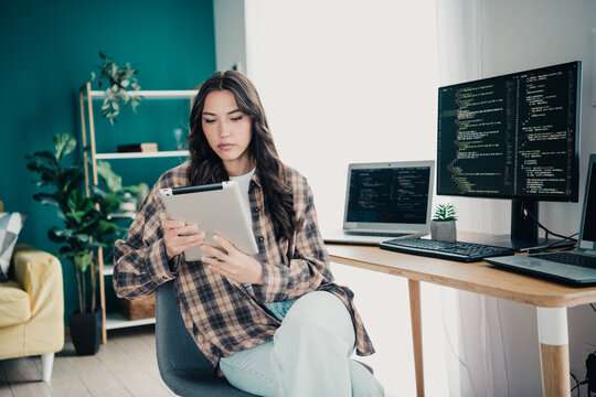 Woman programmer working on a tablet in a home office with multiple computer screens showing code, remote work and focused developer using laptop and desktop monitors for coding and software 