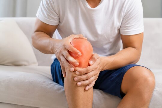 Man holding painful knee joint on couch healthcare medical pain concept.