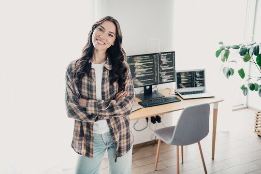 Female programmer smiling with arms crossed in a bright home office, working on code across dual monitors and laptop &mdash; remote developer balancing productivity, confidence and casual tech lifestyle