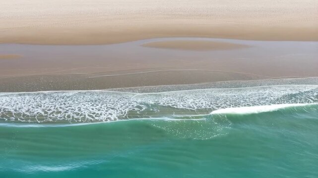 Serene aerial view of gentle ocean waves lapping against a sandy beach. Capturing the tranquility and beauty of coastal nature