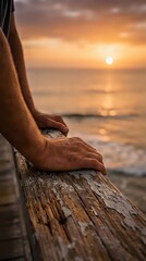 Fototapeta premium Close-up of person's hand resting on weathered wooden pier rail during golden sunset over calm ocean waters. Serene coastal scene for relaxation and travel concepts.