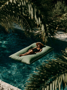Young Woman Relaxing in Inflatable Ring Floating in Blue Swimming Pool With Straw Hat in Lush Mediterranean Summer Resort Setting