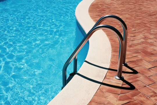 Gleaming metal pool ladder curves into sparkling blue water beside patterned brick