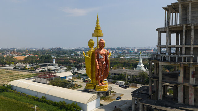 Aerial view of large standing Buddha statues in gold and bronze colors positioned back-to-back under a tiered golden umbrella next to a building frame in Bangkok, Bangkok, Thailand.