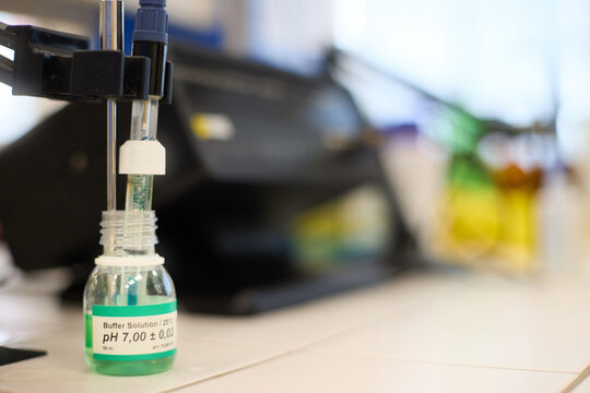 pH meter electrode immersed in buffer solution during laboratory parameter testing, calibration and analytical quality control in an industrial energy lab. Colors: white, green, black.