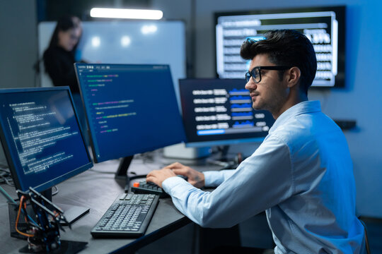 Male Developer Coding At Multiple Monitors In Dark Office
