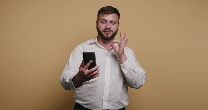 Man shows hand signs while using phone against plain background in a studio