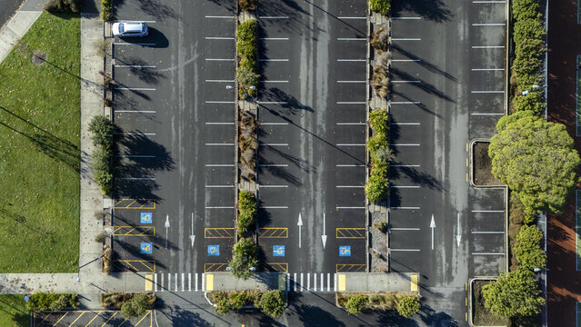 Aerial view of an organized parking lot with a single car, accessible parking bays, and green dividers under bright sunlight Nelson, Nelson Region, New Zealand.