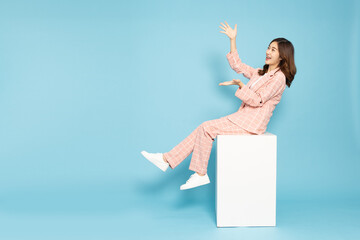 Happy Asian business woman sitting on a white cube, presenting or reaching out her hands. Cheerful...