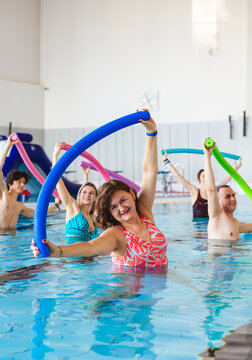 Group of people stretching with colorful noodles during an aqua aerobics class in an indoor swimming pool