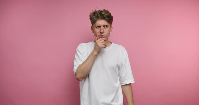 Man thinks while standing against a pink wall in a casual white shirt