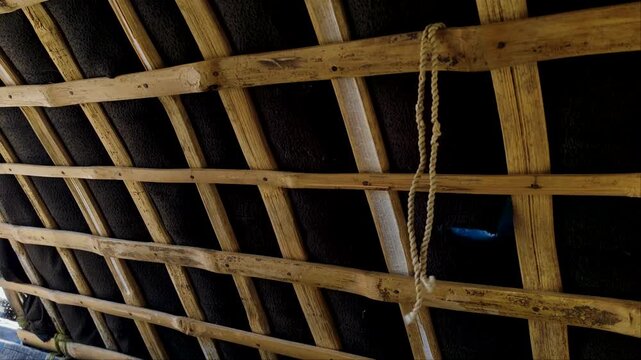 Low angle view of a grid pattern wooden framework with a hanging rope inside a traditional structure