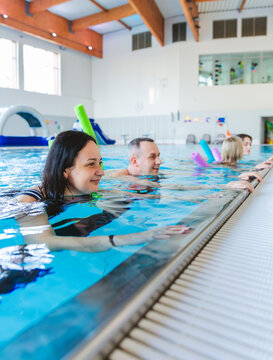 Smiling woman and group of people relaxing at the edge of an indoor swimming pool during an aqua aerobics class