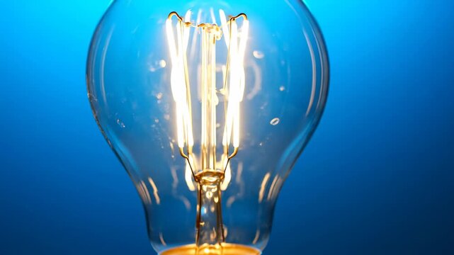 Glowing led edison light bulb close-up with warm filament on blue background electricity