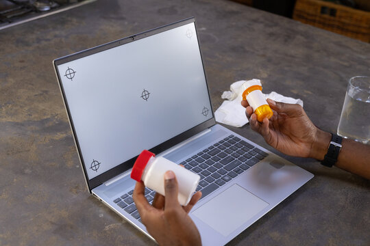 Male comparing pill bottles above laptop with blank screen and calibration marks on kitchen counter