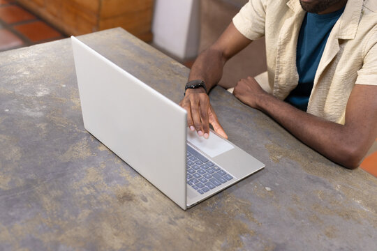 Man working on silver laptop while sitting at worn table wearing black smartwatch, copy space