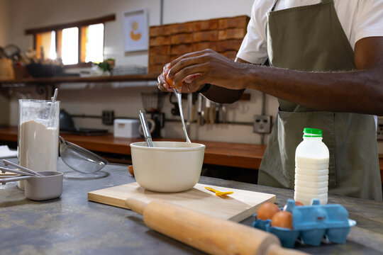 African American man cracking egg and making batter at kitchen counter with mixing bowl, copy space