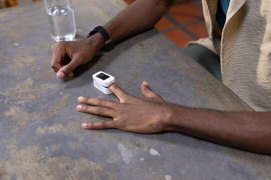 African American man resting hand and adjusting pulse oximeter at kitchen table with water glass