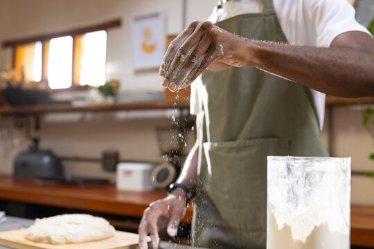 African American man sprinkling flour over dough on kitchen counter wearing green apron flour jar