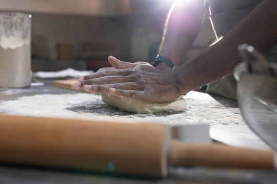Man kneading dough on floured counter, wearing apron and watch, rolling pin blurred in foreground