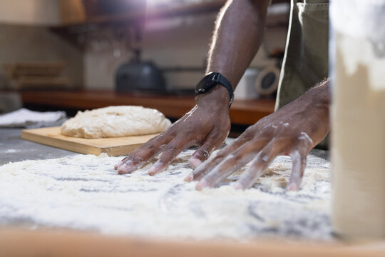 Male kneading dough and spreading flour on floured countertop in kitchen with apron wristwatch