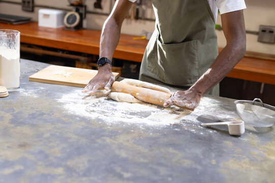 African American man wearing green apron rolling dough on floured counter with wooden rolling pin